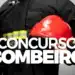 Bombeiro segurando capacete vermelho, vestindo uniforme preto com faixas refletivas amarelas