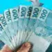 Cédulas de R$ 100 em mãos, representando o pagamento do 13º salário de 2025.