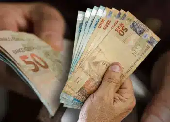 Notas de 50 reais sendo seguradas por uma mão, com destaque para o valor das cédulas.