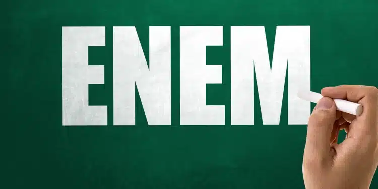 Logotipo grande e branco da palavra ENEM em uma lousa verde-escura, escrito por uma mão com giz branco.