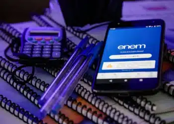 ela do aplicativo ENEM no smartphone mostra a página de login, com materiais de estudo ao redor, incluindo calculadora e cadernos