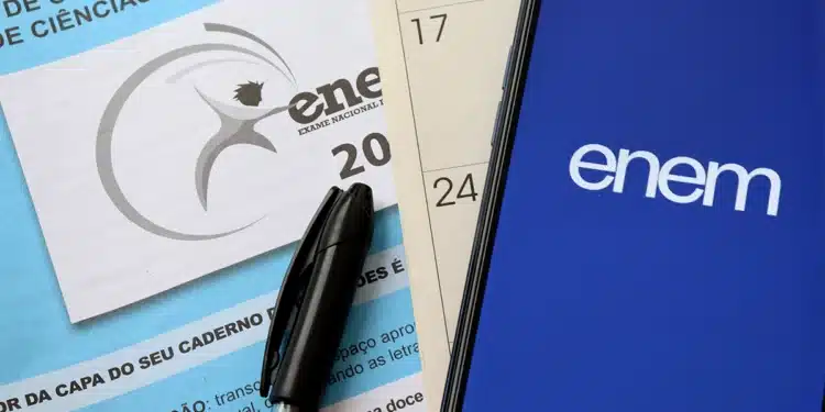 Caderno do ENEM 2025, caneta e celular exibindo logo ENEM." Este texto descreve o conteúdo visual da imagem para usuários com deficiência visual.