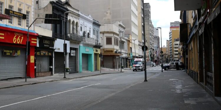 Rua deserta com lojas fechadas e carros de emergência durante um feriado nacional, simbolizando o impacto do descanso no comércio.
