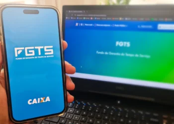 Aplicativo FGTS aberto no celular e site FGTS da Caixa Econômica Federal na tela do computador, ilustrando consulta sobre crédito disponível.