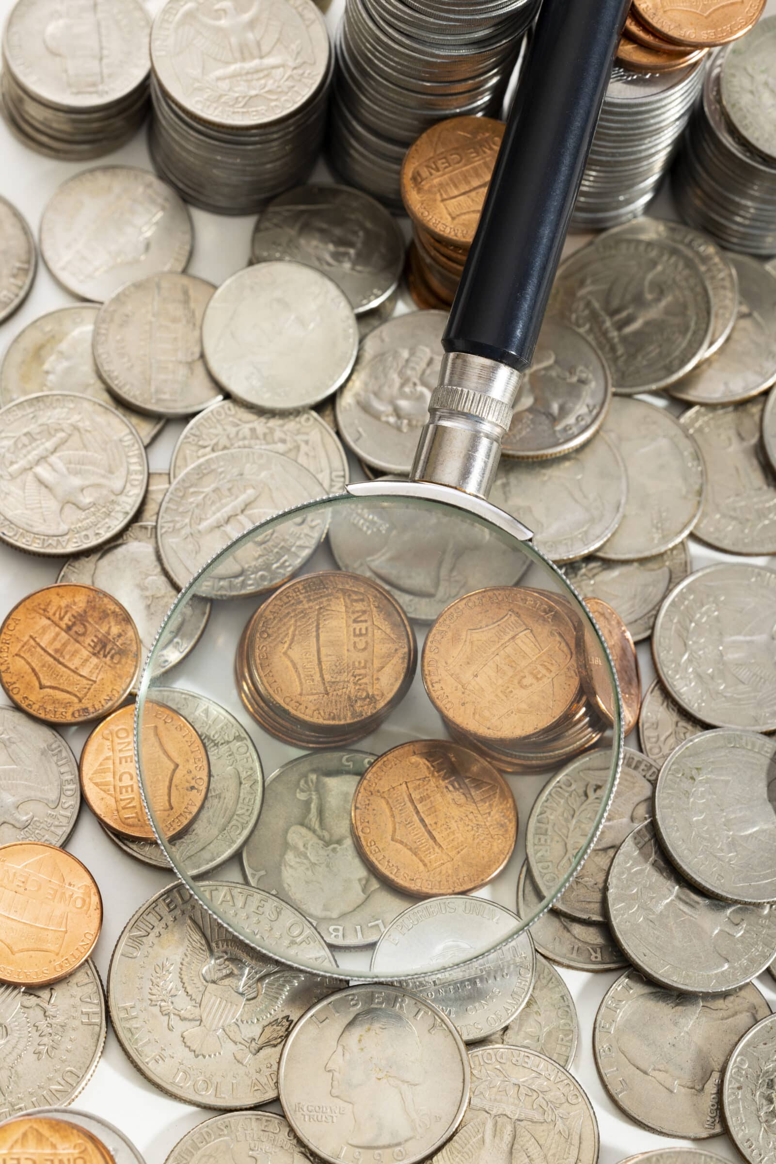 Lupa sobre moedas de diferentes centavos e dólares americanos, simbolizando a inspeção detalhada de peças raras na numismática
