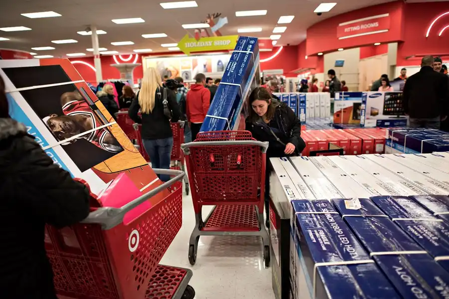 Black Friday: temporada de descontos Clientes lotam uma loja de varejo durante a Black Friday, empurrando carrinhos vermelhos cheios de caixas de eletrônicos e eletrodomésticos.