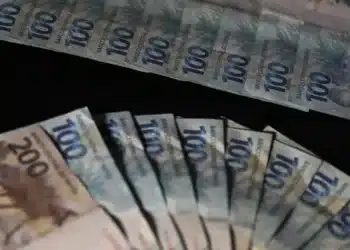 Cédulas de cem e duzentos reais dispostas em leque representando pagamento de R$ 1.518 pela CAIXA e BB.