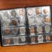 Álbum de moedas aberto sobre mesa de madeira, mostrando organização da coleção com moedas de diferentes países e valores, numismática acessível