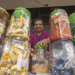 Homem sorridente atrás de potes transparentes cheios de doces embalados à venda em mercado informal.