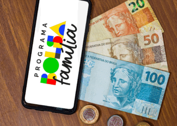 Aplicativo do Programa Bolsa Família ao lado de cédulas de real de 20, 50 e 100 reais.