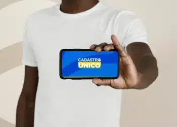 Pessoa exibindo um smartphone com a tela mostrando o logo do CadÚnico, indicando atualização para o ano de 2026.