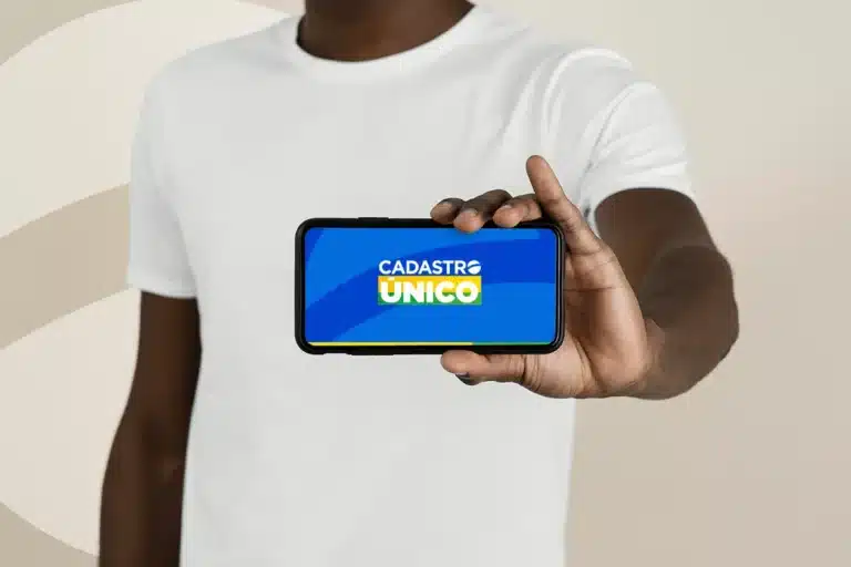 Pessoa exibindo um smartphone com a tela mostrando o logo do CadÚnico, indicando atualização para o ano de 2026.