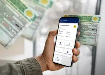 Pessoa acessando informações da CNH pelo aplicativo do Detran, com documentos físicos ao fundo.