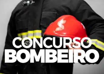 Bombeiro segurando capacete vermelho com uniforme preto refletivo em fundo cinza