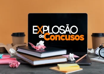 Notebook com a frase Explosão de Concursos, livros, papel amassado e relógio em mesa de estudo.