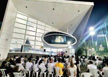 Fachada iluminada da Nave do Conhecimento durante evento noturno com público ao ar livre.