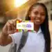 Estudante feliz mostrando cartão Pé-de-Meia, programa de poupança do ensino médio, com pagamento de R$ 200 e benefício extra em dezembro.
