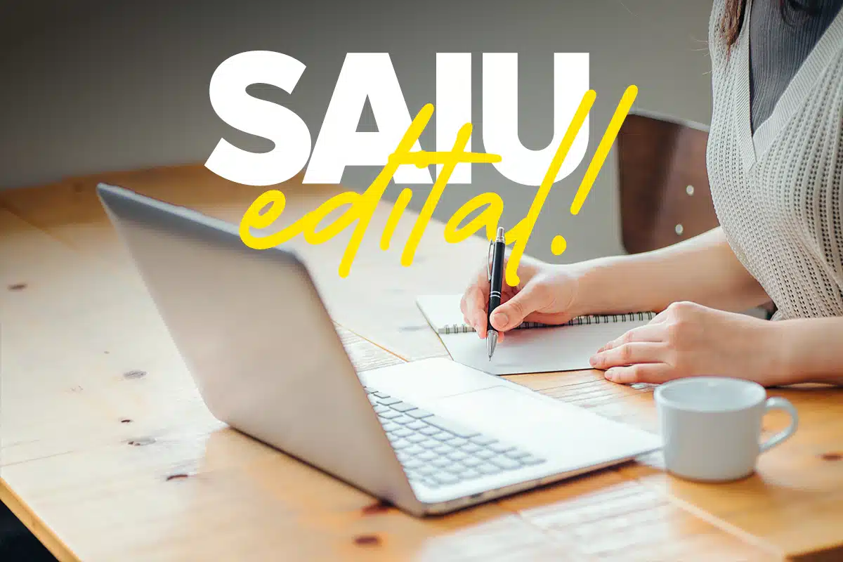 Pessoa anotando informações ao lado de notebook sobre abertura de inscrições de edital da prefeitura.