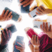 Pessoas formando círculo segurando diferentes smartphones modernos em várias cores.