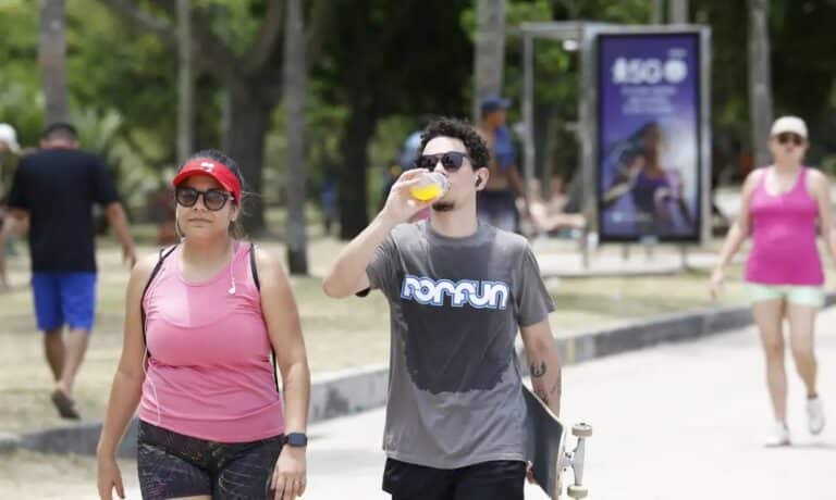 Pessoas andando ao ar livre sob altas temperaturas, demonstrando a importância da hidratação e da proteção contra o calor no verão