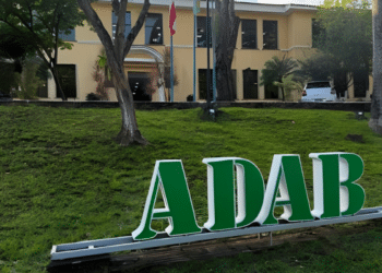 Letreiro verde com as letras ADAB na fachada de prédio institucional cercado por árvores e área verde