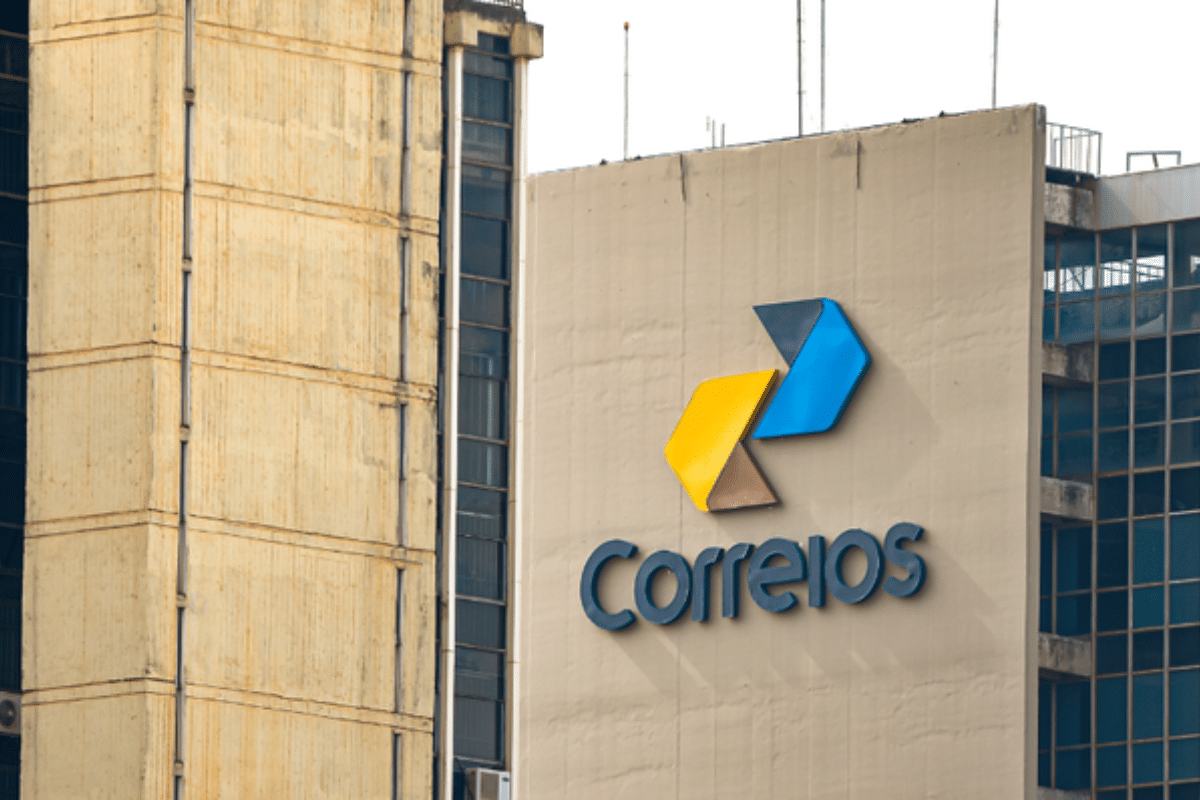 Logotipo dos Correios com setas azul e amarela no muro externo de um prédio administrativo