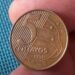 Close detalhado de uma moeda de 5 centavos de real do ano 2002, exibindo o número 5 e a data, segurada entre os dedos sobre um fundo azul texturizado.