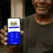 Homem segurando smartphone exibindo tela do Programa Bolsa Família, com logo e opções de menu em aplicativo