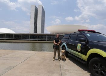 Policial Legislativa Federal ao lado de viatura e cão farejador em frente ao Congresso Nacional em Brasília