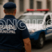 Guarda municipal de costas com uniforme azul e viatura ao fundo representando concurso público para a corporação.