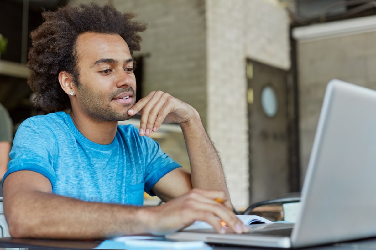 Jovem pesquisando informações sobre concurso público no notebook para se inscrever.