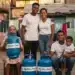 Família feliz em comunidade recebendo botijões de gás do programa social Gás do Povo