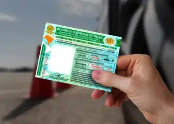 CNH brasileira em mãos, com fundo desfocado e cones de sinalização ao fundo.