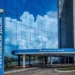 Fachada do prédio do INSS com reflexo do céu e nuvens no vidro, com o letreiro 'Previdência Social' em destaque, indicando o local de atendimento do Instituto Nacional do Seguro Social.