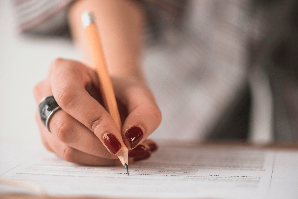 Mão feminina escrevendo em formulário com lápis, documento em papel