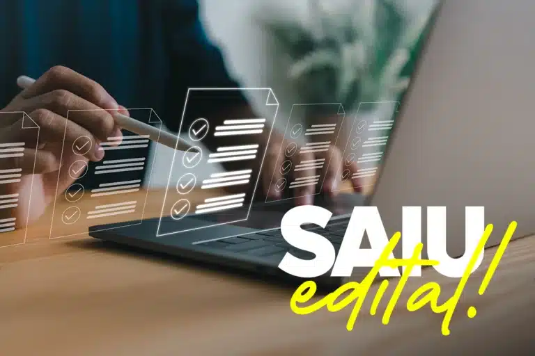 Pessoa usando notebook ao lado de documentos digitais com a frase "SAIU edital!".