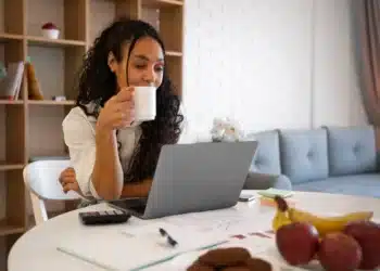 Profissional de home office trabalhando com computador e café, simbolizando as profissões com maiores oportunidades no mercado de trabalho em 2026.