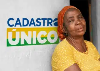 Mulher em primeiro plano, com o fundo exibindo a logo do CadÚnico, ilustrando as novas regras do CadÚnico para famílias unipessoais.