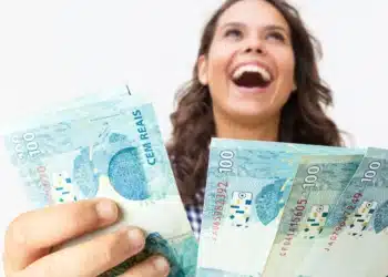 Mulher sorrindo segurando notas de R$100, representando o pagamento da Caixa Econômica Federal para a última rodada de janeiro de 2026.