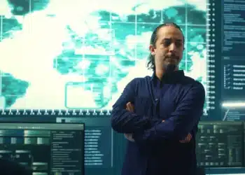 Homem analisando dados em frente a um monitor com mapa mundial, representando as carreiras em alta para 2026.