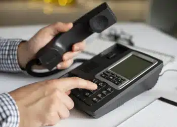 Pessoa utilizando um telefone fixo, ilustrando a atualização nos prefixos DDD que entram em vigor em fevereiro de 2026.