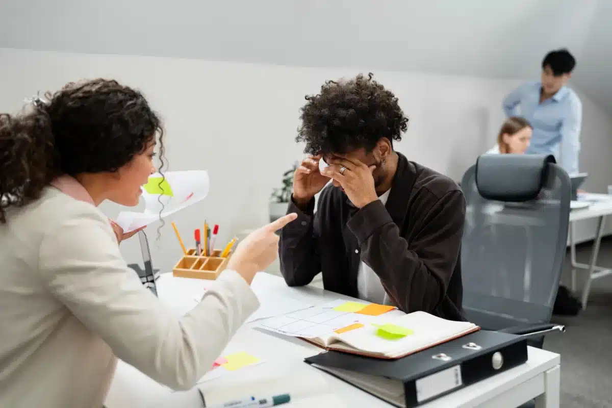 Colaboradores em conflito durante uma discussão no ambiente de trabalho, com um dos colegas demonstrando estresse enquanto outro aponta para ele.