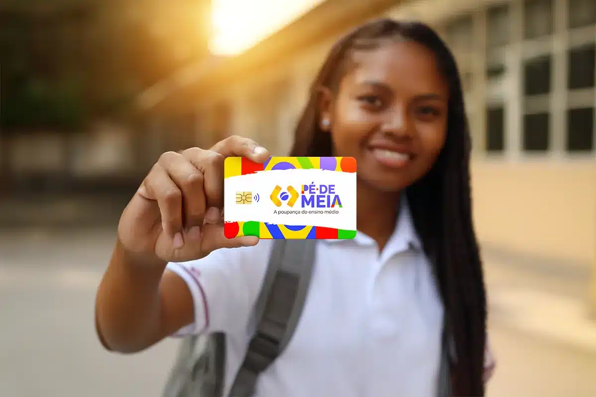 Estudante exibe cartão do programa Pé-de-Meia 2026 Jovem segurando cartão colorido do programa Pé-de-Meia com uniforme escolar e mochila