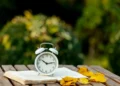 Relógio de alarme sobre livro com folhas de outono, representando o possível horário de verão 2026 no Brasil