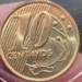 Close de uma moeda de 10 centavos de Real do ano 2000, protegida por uma cápsula de acrílico transparente, mostrando o número 10 e o ano de cunhagem com clareza.