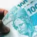 Cédulas de 100 reais do Brasil em mãos, relacionada ao projeto sobre parcelas extras no seguro-desemprego.