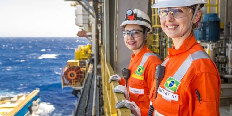 Duas funcionárias da Petrobras usando uniforme laranja e capacete em plataforma de petróleo no mar