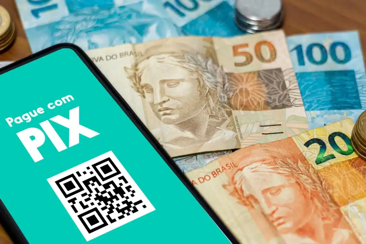 Pix não é tributado: entenda como funciona o Imposto de Renda. Tela de celular exibindo QR Code do Pix sobre cédulas de real, ilustrando que transferências via Pix não são tributadas pelo Imposto de Renda.