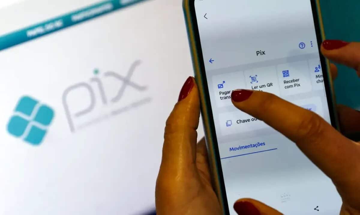 Pessoa utilizando o aplicativo do Pix no celular, com destaque para a tela de pagamentos e o logotipo do sistema ao fundo.