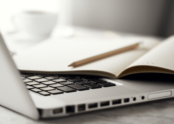Caderno aberto com lápis repousa sobre teclado de notebook em mesa clara